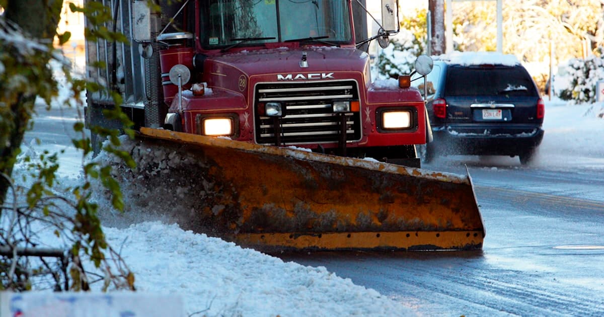 A snow plow driving down a snow covered road